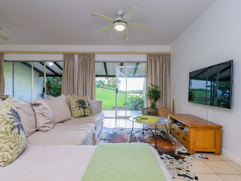 Bright living room featuring tiled flooring, a ceiling fan, and large sliding glass doors providing direct access to the outdoor patio and garden area.