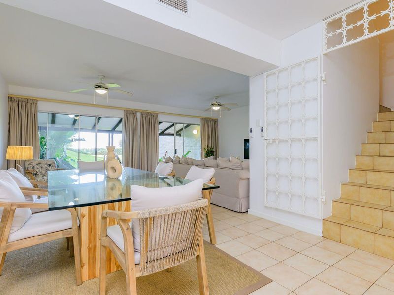 Open plan living and dining area featuring tiled floors, ceiling fans, and a staircase with decorative metal security gate leading to the upper level.