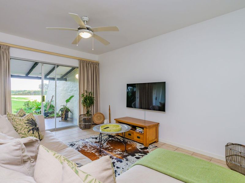 A bright living room featuring tiled flooring, a ceiling fan, and large sliding glass doors that provide direct access to the outdoor patio area.