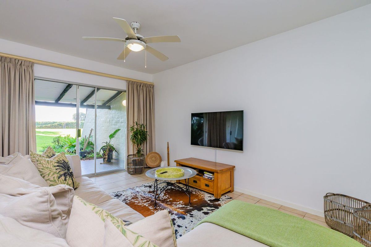 A bright living room featuring tiled flooring, a ceiling fan, and large sliding glass doors that provide direct access to the outdoor patio area.