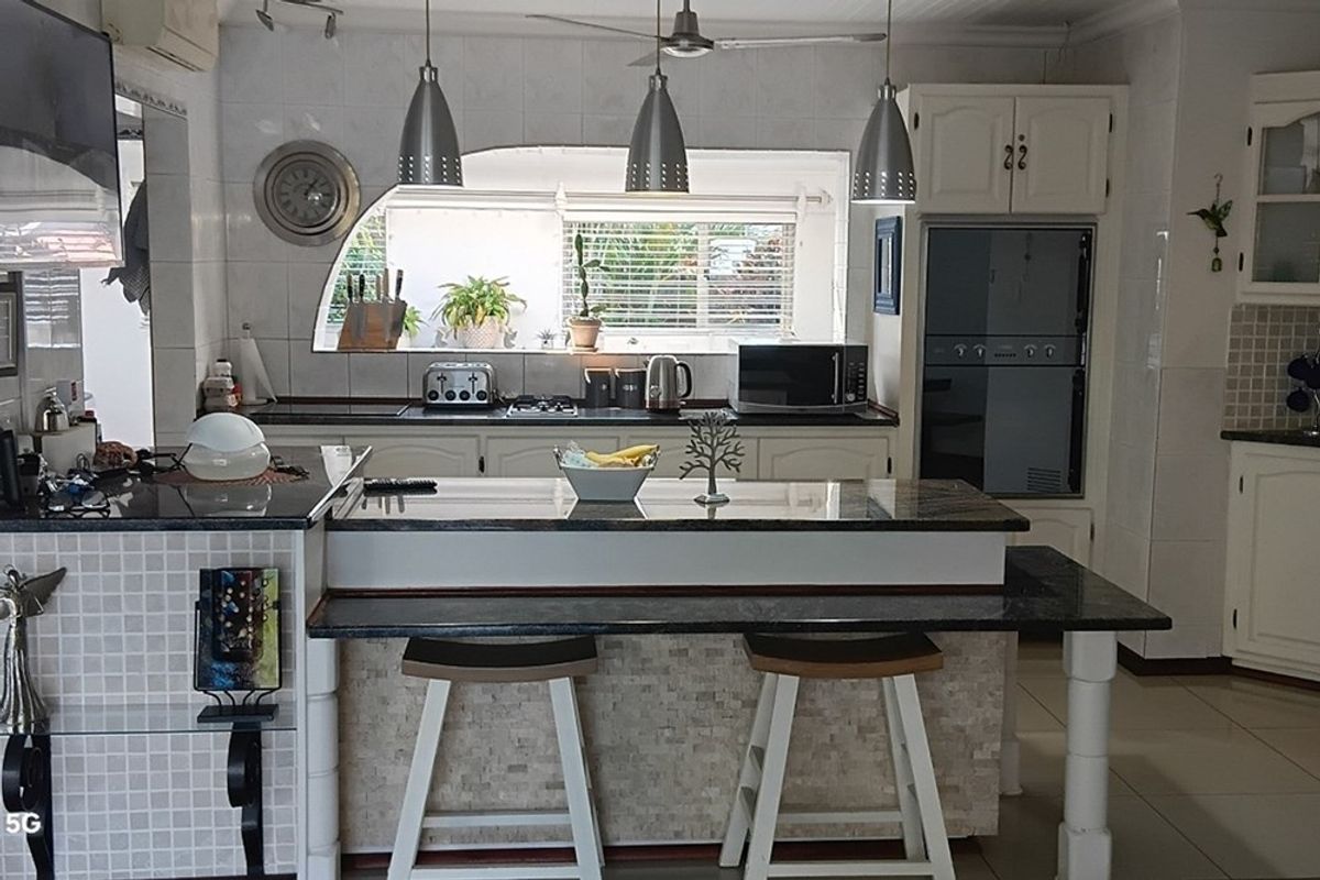 A functional kitchen featuring granite countertops, a central breakfast bar, built-in oven, and tiled splashbacks with ample storage cabinetry.