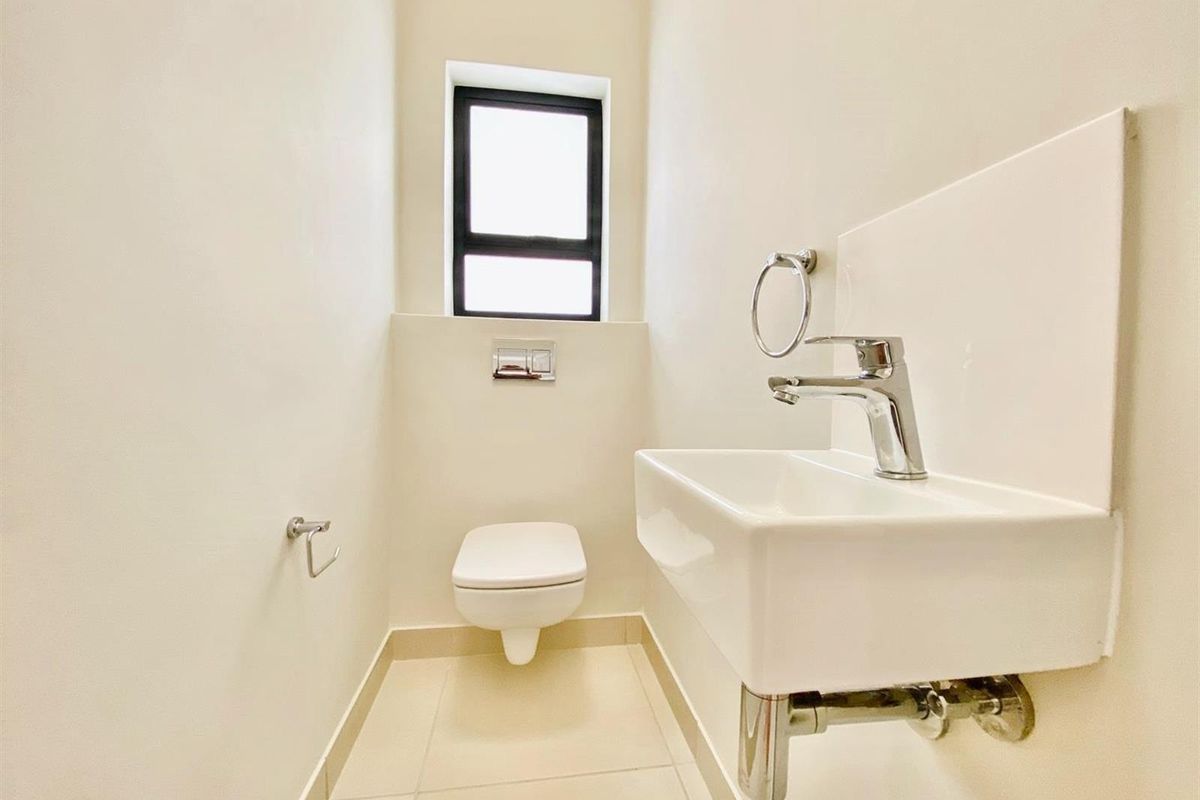 A clean and modern guest cloakroom featuring a wall-mounted toilet, a compact basin with chrome fixtures, and neutral floor tiling.