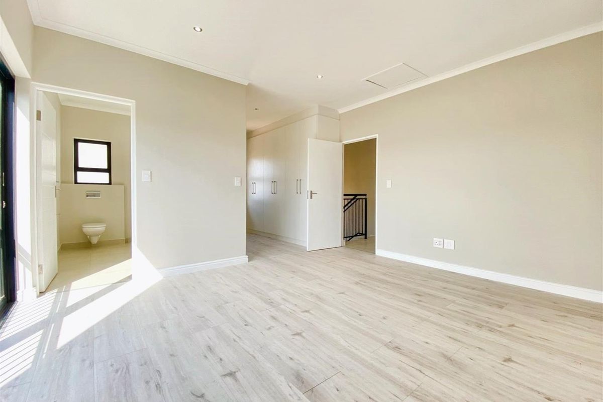 Spacious bedroom featuring light wood-look flooring, built-in cupboards, and an en-suite bathroom with modern fixtures.