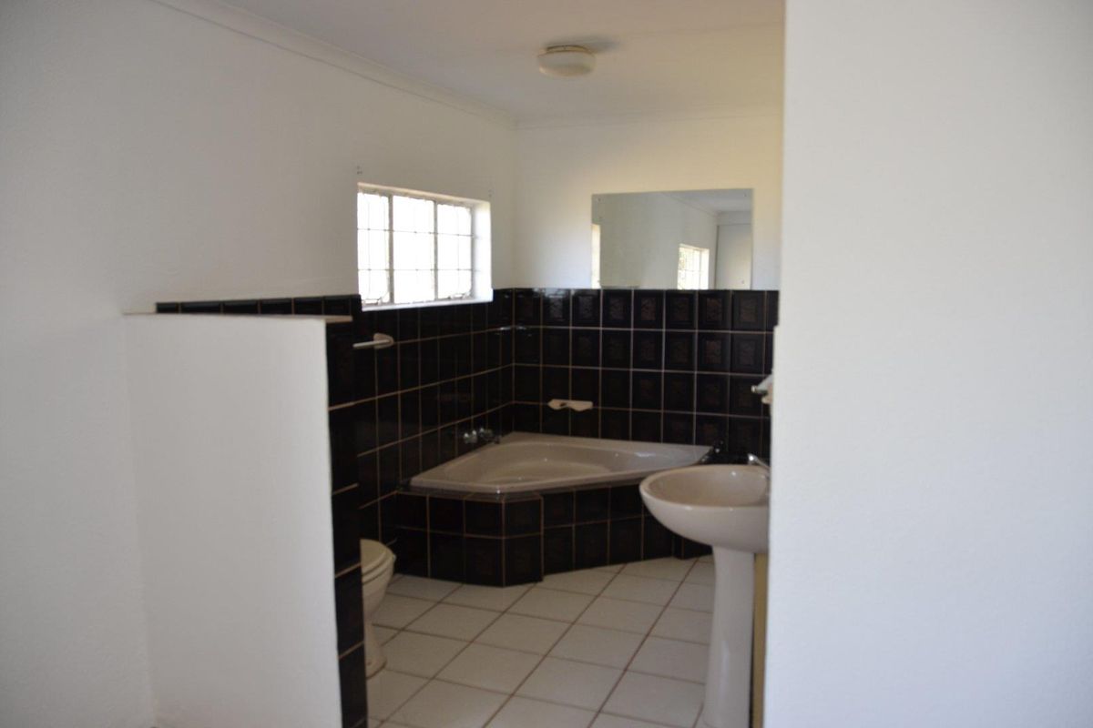 A functional bathroom featuring a corner bathtub, pedestal basin, and dark tiled wall finishes.