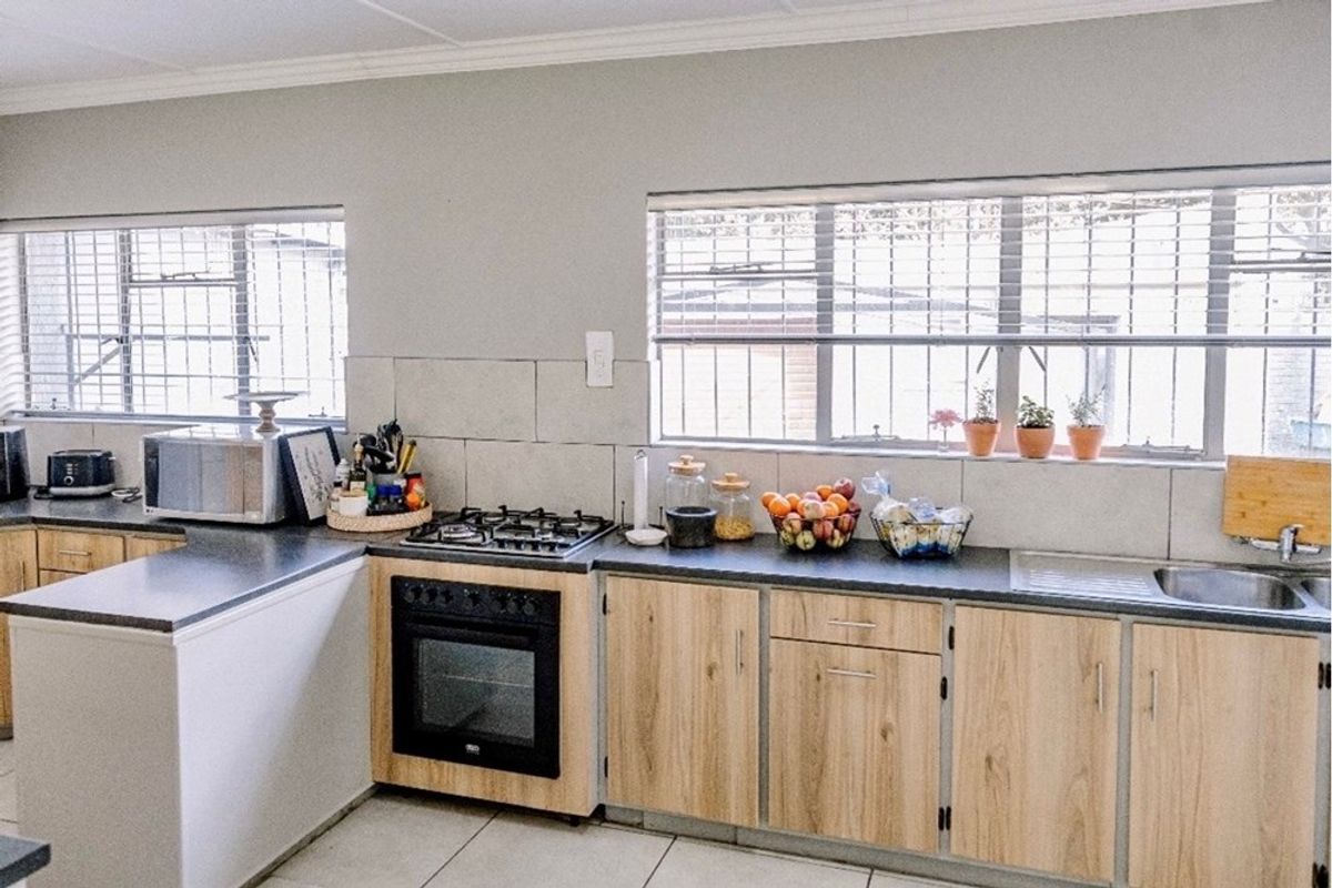 Functional kitchen featuring light wood-finish cabinetry, dark laminate countertops, a built-in oven with gas hob, and large windows providing natural light.