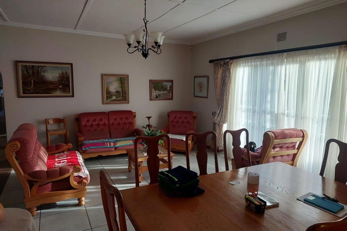 A spacious living and dining area featuring tiled flooring, a classic chandelier, and large windows allowing for natural light.