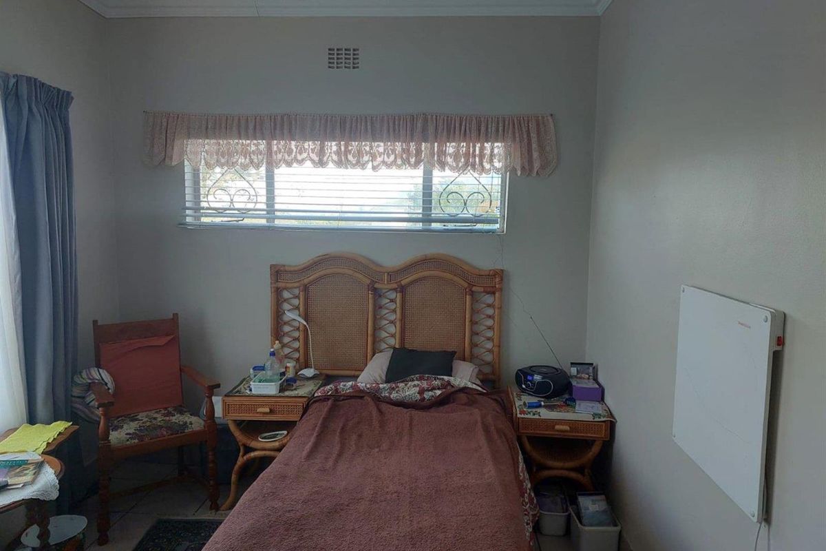 A functional bedroom featuring tiled flooring, a horizontal window with security bars, and a wall-mounted electric heater.