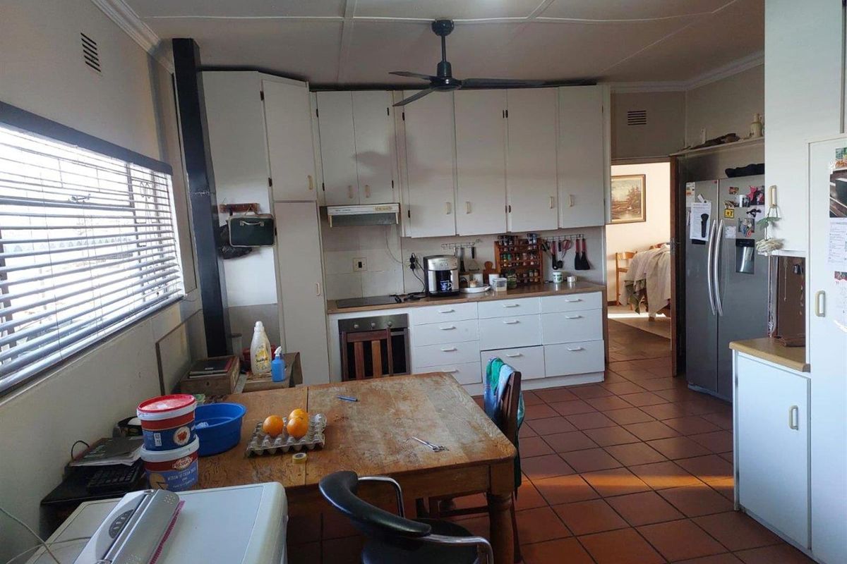 A functional kitchen featuring white cabinetry, built-in oven and hob, extractor fan, and tiled flooring, with an adjacent dining area.