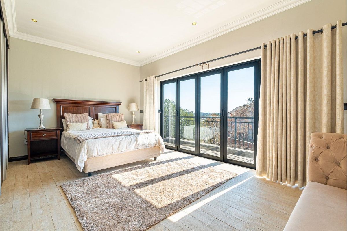 Spacious bedroom featuring light-toned tiled flooring, elegant cornicing, and large black aluminium stacker doors opening onto a private balcony with scenic views.