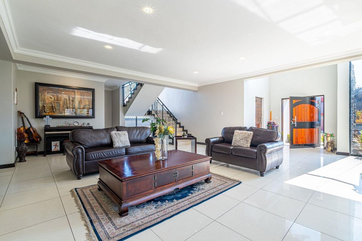 Spacious open-plan living area featuring polished tiled floors, recessed lighting, and a feature staircase with a decorative metal balustrade.