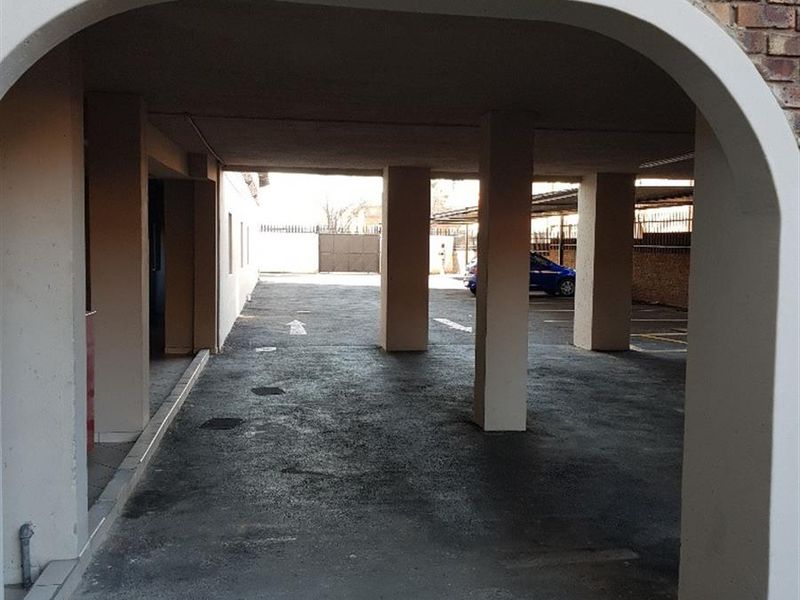 A covered parking area featuring a brick facade, arched entrance, and concrete support pillars with an asphalt driveway.