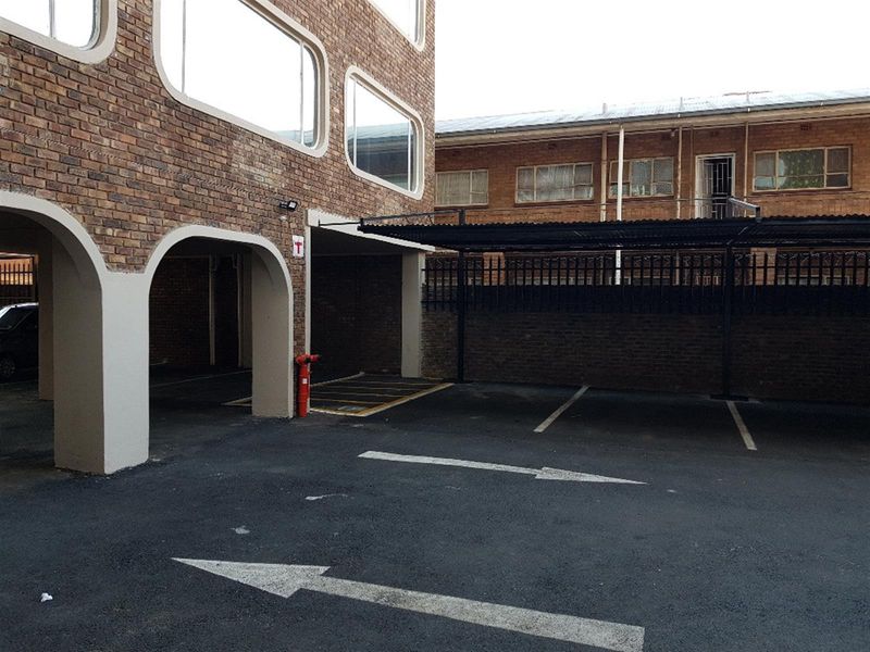 Exterior view of the apartment complex featuring a brick facade, covered parking bays, and an asphalt driveway with marked directional arrows.