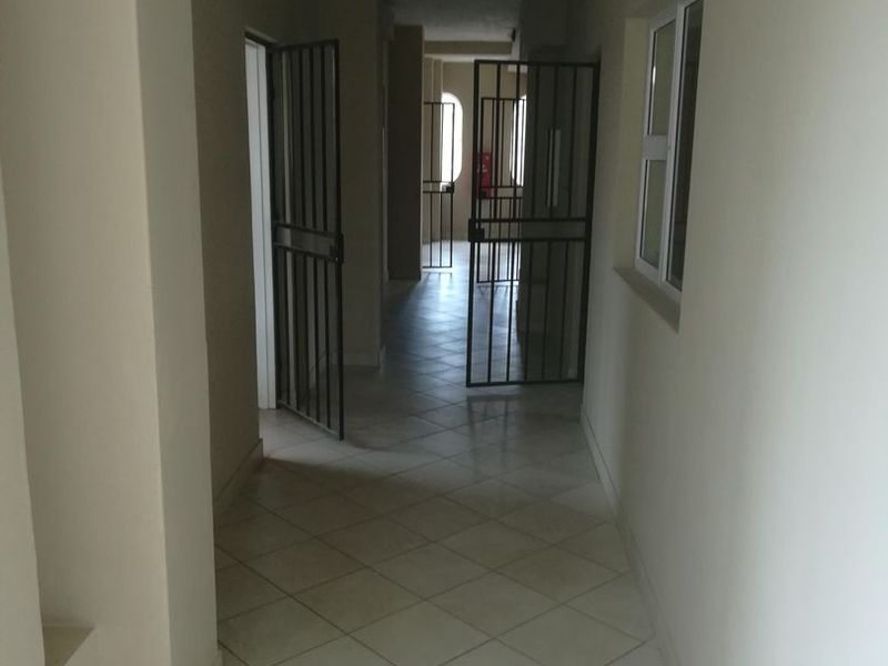 A functional apartment hallway featuring tiled flooring and security gates leading to adjacent rooms.