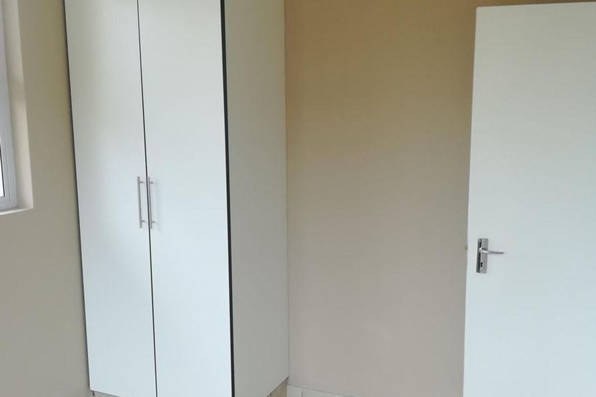 A clean, empty bedroom featuring neutral wall paint, tiled flooring, and a built-in white wardrobe.