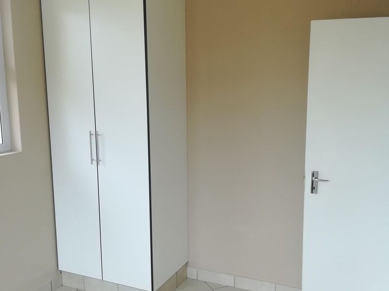 A clean, empty bedroom featuring neutral wall paint, tiled flooring, and a built-in white wardrobe.