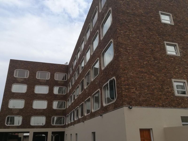 A view of the apartment building exterior featuring a brick facade with distinctive rounded-corner windows and a concrete ground level.