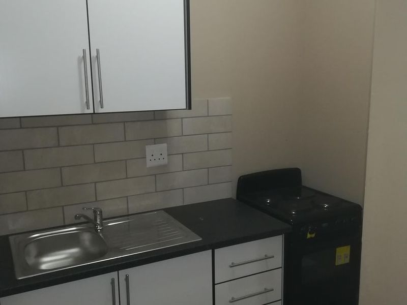 A compact, modern kitchen featuring white cabinetry, a stainless steel sink, subway tile backsplash, and a built-in electric stove.