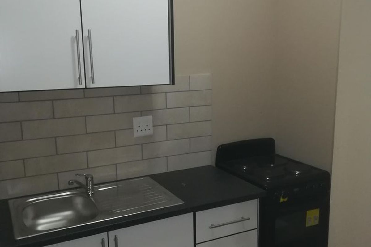 A compact, modern kitchen featuring white cabinetry, a stainless steel sink, subway tile backsplash, and a built-in electric stove.
