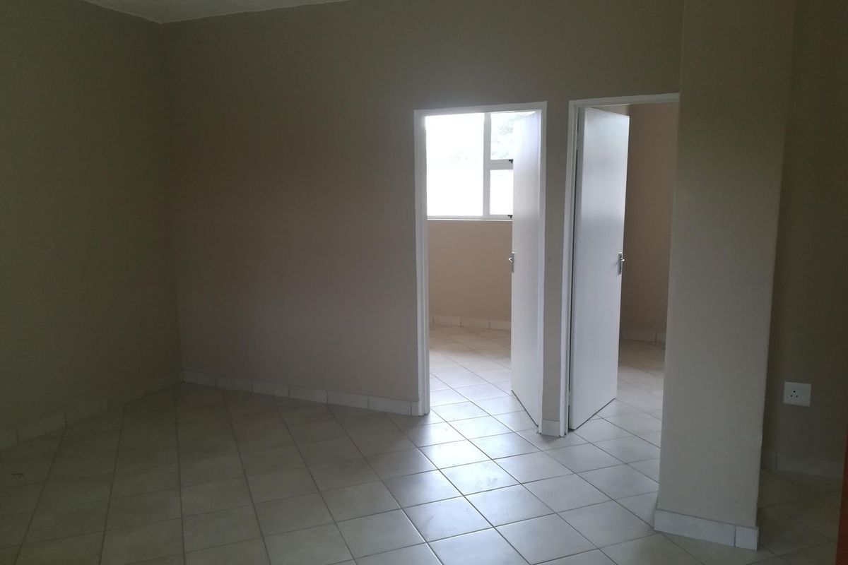 An empty, neutral-toned living area featuring ceramic floor tiles and access to adjacent rooms through two doorways.