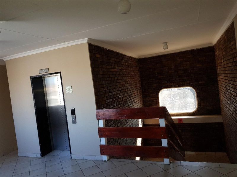 Apartment building hallway featuring a brick accent wall, elevator access, and a staircase with a wooden railing.