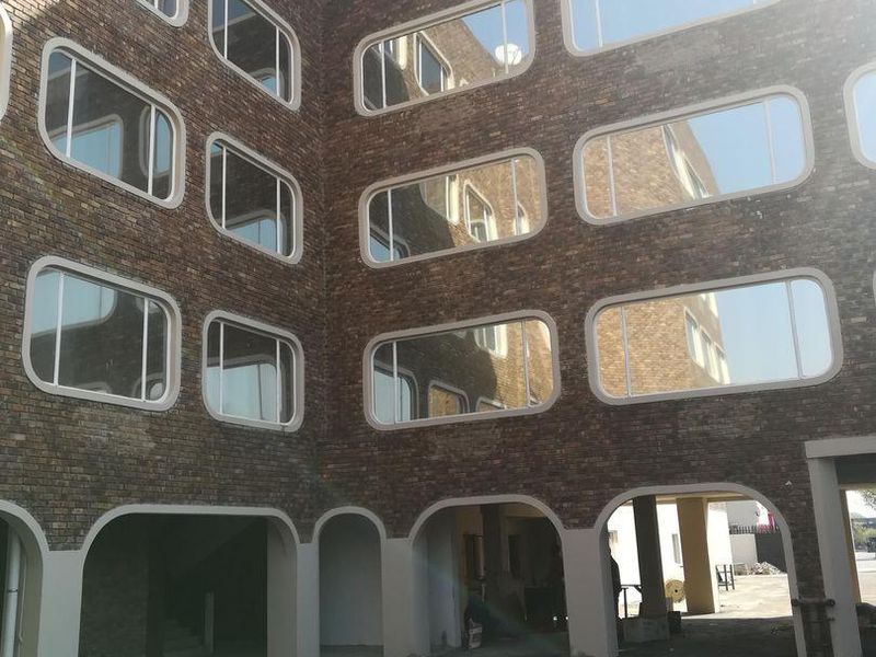 Exterior view of an apartment building featuring a brick facade with distinctive rounded rectangular windows and arched ground floor access points.