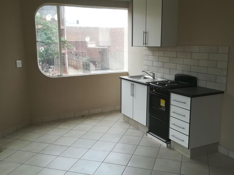 A compact kitchen featuring built-in cabinetry, a stainless steel sink, a freestanding stove, and a large window providing natural light.
