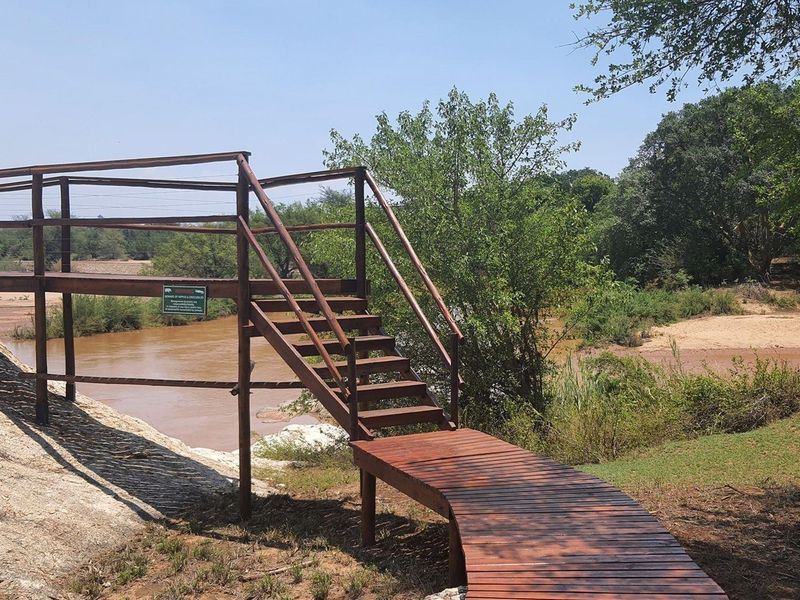 A scenic view of a riverbank featuring a well-maintained wooden boardwalk and staircase structure, providing access to the natural landscape.