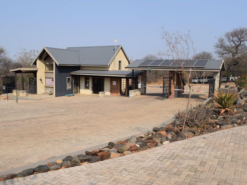 A well-maintained residential estate entrance featuring a paved driveway, security gatehouse with solar panels, and attractive stone landscaping.