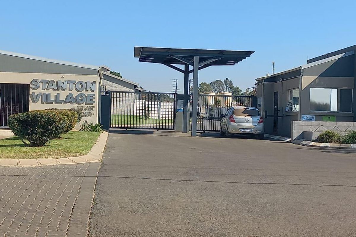 The entrance to Stanton Village townhouse complex featuring a secure gated access point, guard house, and paved driveway.