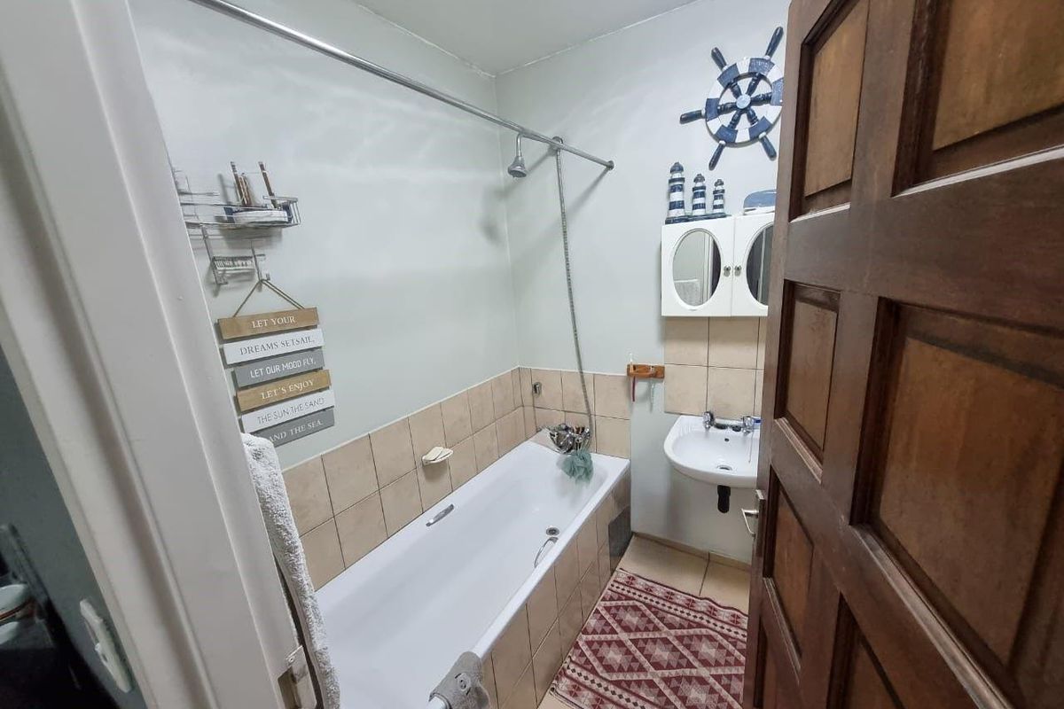 A functional bathroom featuring a bathtub with shower attachment, wall-mounted basin, and neutral tiled finishes.