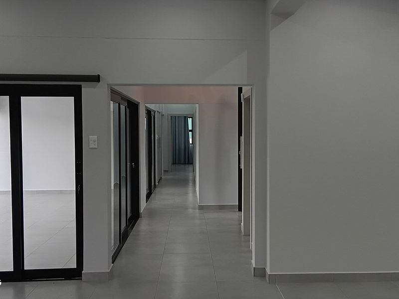 A clean, modern hallway featuring neutral tiled flooring and multiple sliding glass doors providing access to adjacent rooms.