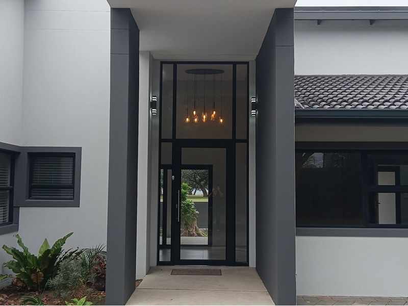 Modern front entrance featuring a covered porch, sleek glass door, and contemporary dark-framed windows with a tiled roof.
