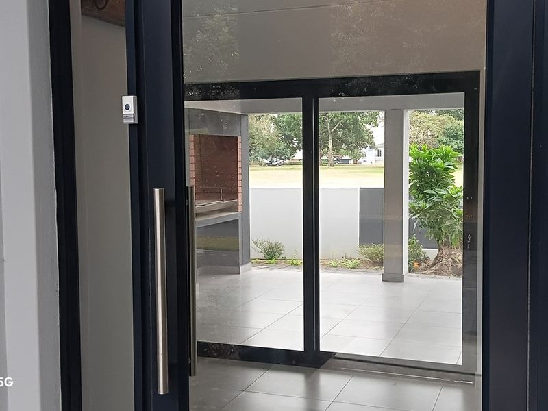 A covered patio area featuring tiled flooring, a built-in braai, and large sliding glass doors providing access to the garden.