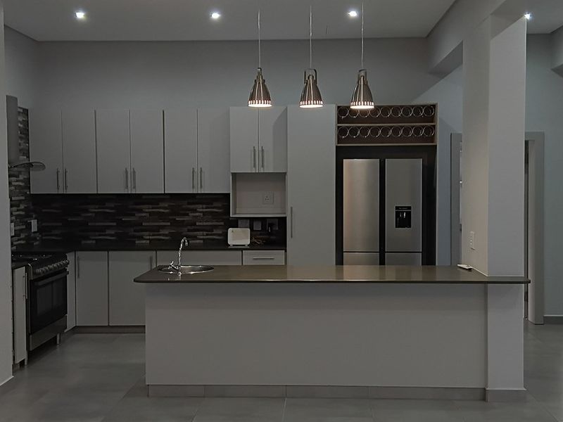 Modern kitchen featuring sleek cabinetry, stone countertops, a central island, stainless steel appliances, and stylish pendant lighting in an open-plan layout.