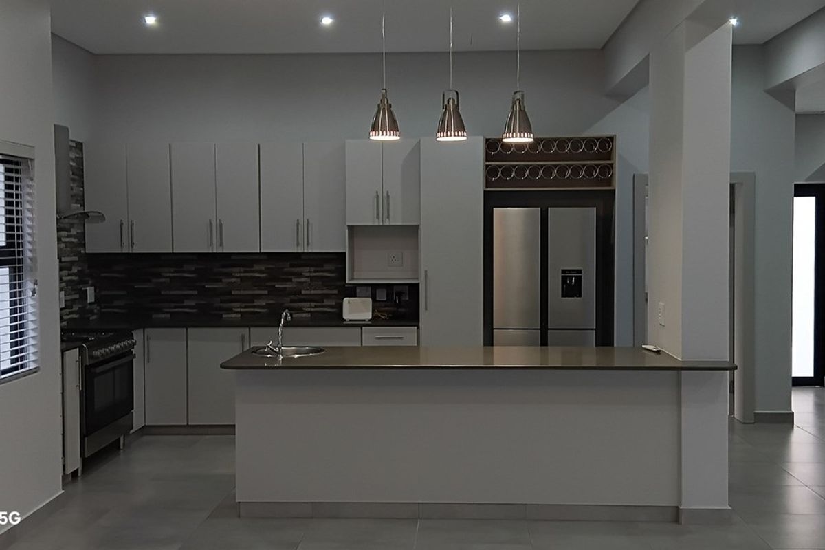 Modern kitchen featuring sleek cabinetry, stone countertops, a central island, stainless steel appliances, and stylish pendant lighting in an open-plan layout.