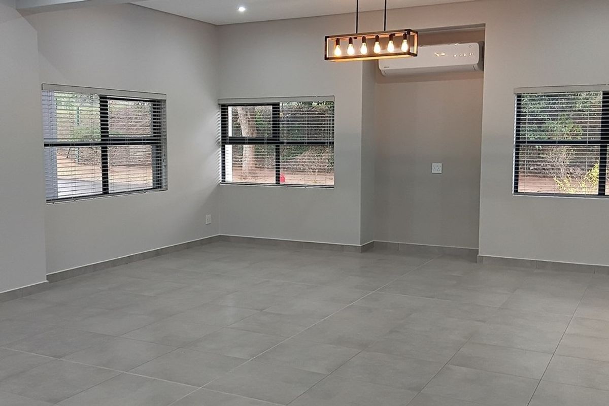 A bright, open-plan living area featuring neutral tiled flooring, modern recessed lighting, a stylish pendant fixture, and a wall-mounted air conditioning unit.