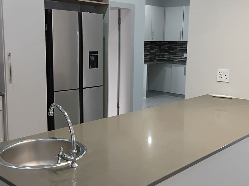 Modern kitchen featuring a central island with a stone countertop, integrated sink, and clean cabinetry, with a secondary scullery area visible in the background.