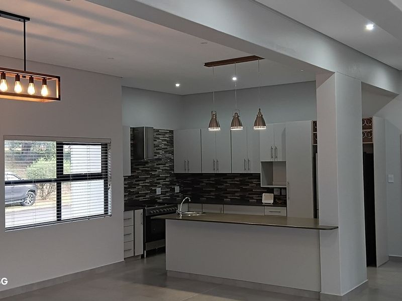 Modern open-plan kitchen featuring a central island, sleek cabinetry, stone splashback, and contemporary pendant lighting, seamlessly integrated into the living space.