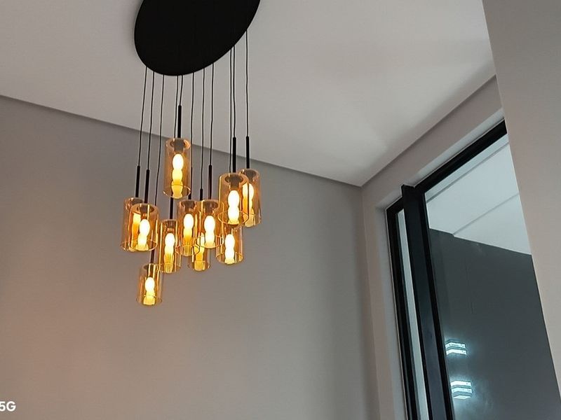 A close-up view of a modern multi-pendant light fixture with glass shades and a black window frame in a neutral-toned room.