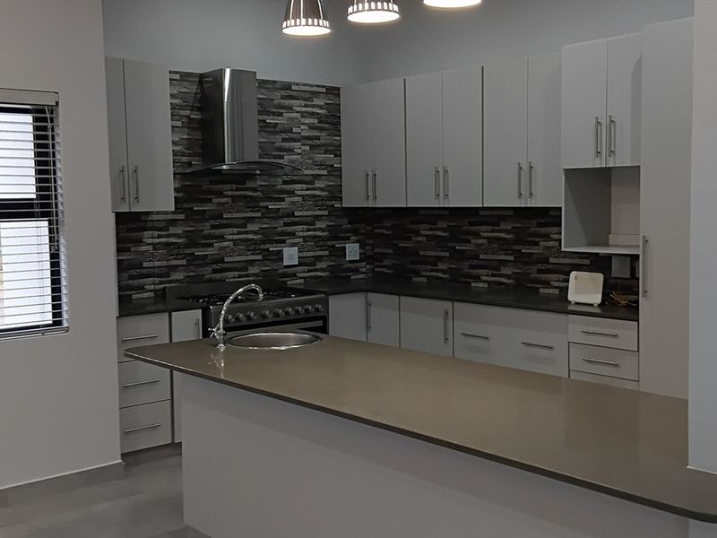 Modern kitchen featuring a central island with an undermount sink, stone-look backsplash, stainless steel extractor fan, and ample built-in cabinetry.