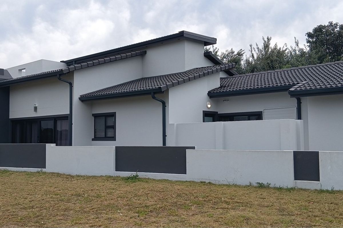 A modern residential exterior featuring a clean, neutral facade, tiled roof, and a low-maintenance boundary wall with integrated outdoor lighting.