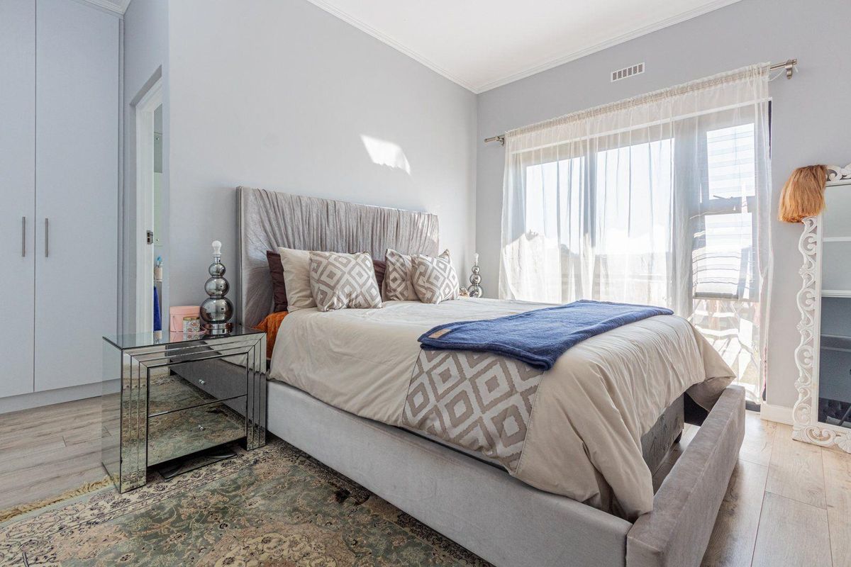 A bright bedroom featuring built-in cupboards, light wood-look flooring, and large sliding glass doors that provide access to an outdoor area.