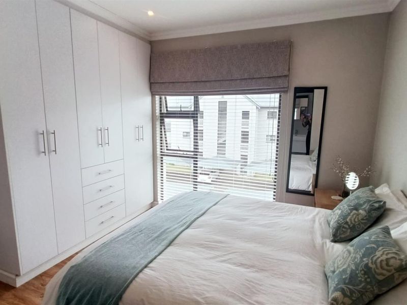 A well-maintained bedroom featuring ample built-in cupboard storage, laminate flooring, and a window fitted with venetian blinds.