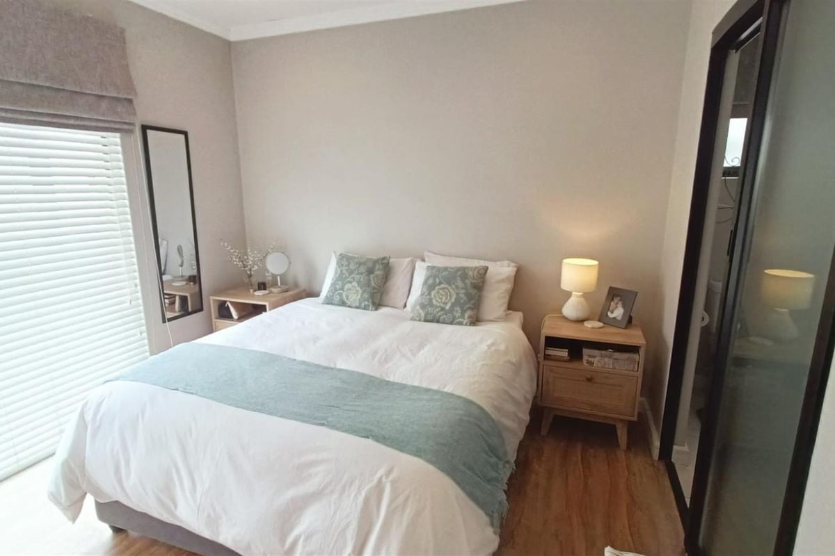 A well-maintained bedroom featuring laminate flooring, neutral wall tones, and a sliding door with venetian blinds for natural light control.