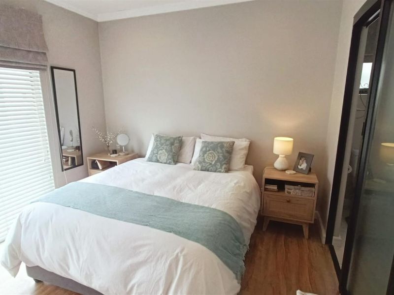 A well-maintained bedroom featuring laminate flooring, neutral wall tones, and a sliding door with venetian blinds for natural light control.