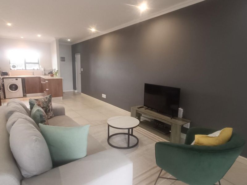 Open-plan living area featuring tiled floors, recessed lighting, and a functional kitchen space with integrated laundry facilities.