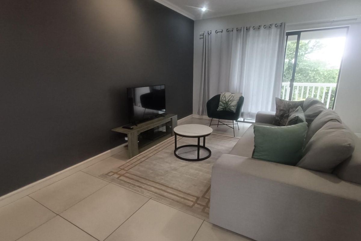 A modern living room featuring large format floor tiles, a dark accent wall, and a sliding glass door providing access to an outdoor balcony.