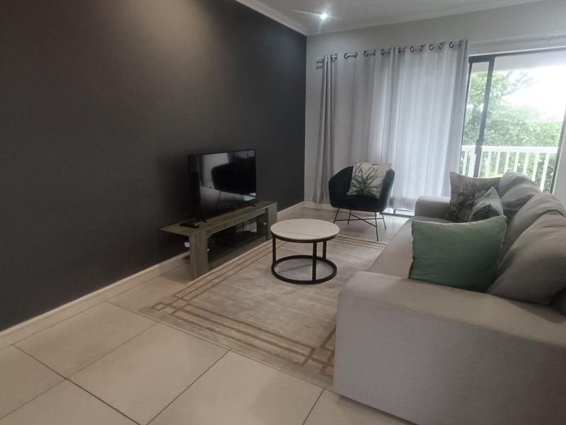 A modern living room featuring large format floor tiles, a dark accent wall, and a sliding glass door providing access to an outdoor balcony.