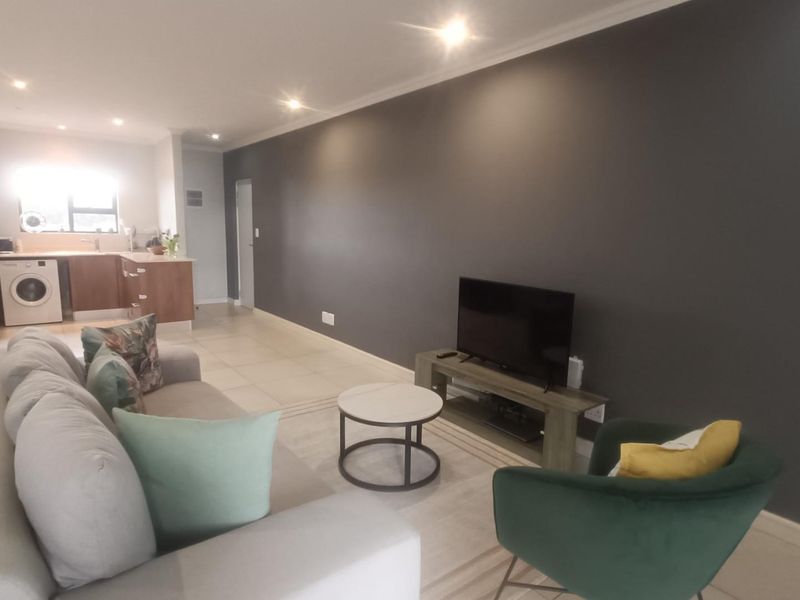 An open-plan living area featuring tiled floors, recessed lighting, and a functional kitchen space with built-in cabinetry and laundry plumbing connections.