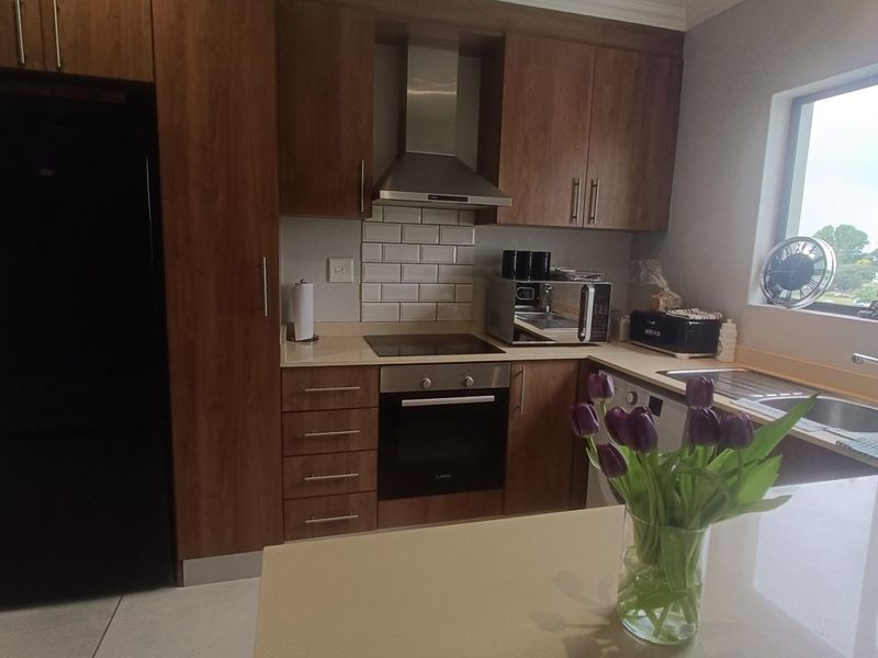 Modern kitchen featuring wood-finish cabinetry, stone countertops, subway tile backsplash, and integrated stainless steel appliances including an oven and hob.